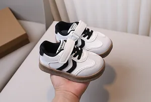 Detail view of children's white sneakers with black stripes and brown gum sole
