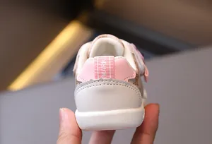 Dettaglio ravvicinato di scarpe primi passi beige con suola morbida e motivo logato vintage
