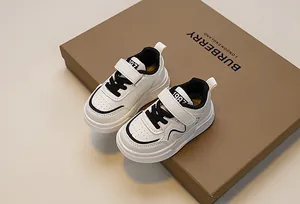 Detail view of white kids' sneakers with black laces, velcro strap and 1987 print