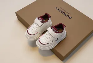 Macro view of kids sneakers featuring white leather with burgundy trim and velcro closure