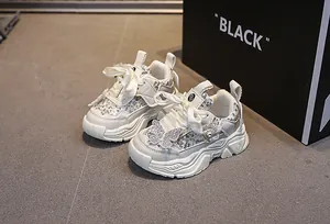 Detail of girls' white chunky sneakers featuring silver sequins and a jeweled ribbon bow