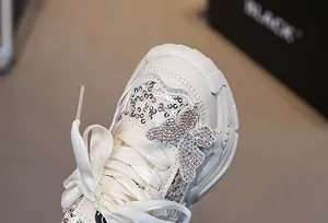 Detailed macro view of white girls sneakers featuring shiny sequins and a rhinestone butterfly