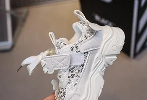 Detail of girls' chunky platform sneakers featuring silver sequins and a large ribbon bow