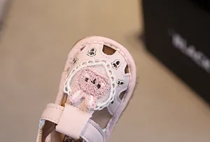 Dettaglio sandalo rosa per neonata con cuore in pizzo, coniglio di peluche e pelle traforata