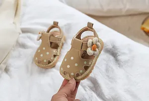 Détail d'une sandale kaki pour bébé avec des pois blancs et un ornement floral en tissu