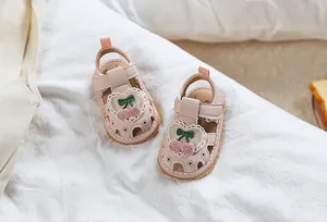 Detail of pink baby sandals with crochet cherry decor on white cotton cloth