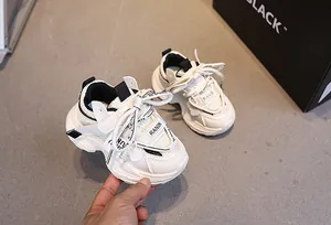 Detail of kids white sports sneakers with velcro strap and breathable mesh on gray floor