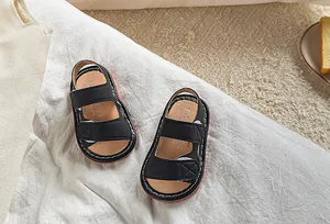 Détail de sandales noires pour bébés avec double bride velcro et bord de semelle rouge