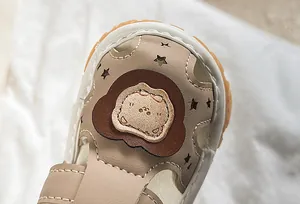Macro shot of khaki baby sandals featuring cartoon animal patch and star-shaped cutouts