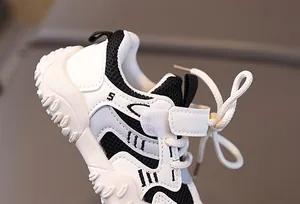 Detail view of children's white athletic shoes featuring breathable mesh and velcro straps