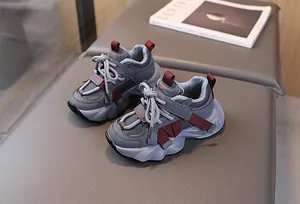 Detail of grey kids chunky sneakers with mesh panels and burgundy accents on leather bench