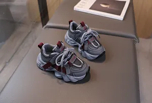 Detail of dark grey kids sneakers with burgundy accents on a soft grey textured surface