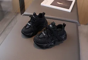 Detail view of black kids chunky sneakers with leather mesh panels on a modern gray backdrop