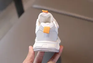 Close-up of kids sports sneakers featuring white leather, grey suede heel, and orange pull tabs
