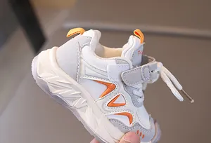 Detail of kids' white and grey sneakers with orange accents and Velcro strap closure