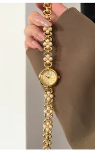 Detail of elegant gold quartz watch featuring white pearl chain strap and Roman numerals
