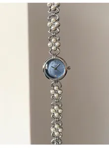 Macro detail of silver floral watch band with white pearls and blue pearlescent dial