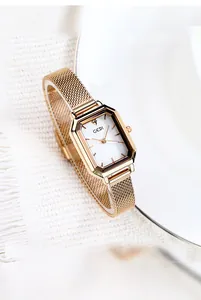 Macro detail of octagonal rose gold watch with mesh strap on a soft fabric backdrop