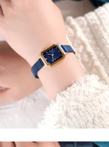 Elegant gold rectangular watch with blue sunray dial and blue mesh strap on wrist