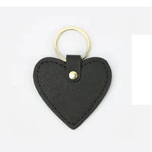Detail of a black heart-shaped PU leather keychain with cross pattern and gold metal ring