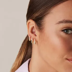Three gold huggie hoop earrings with micro-set zircons on a model's ear