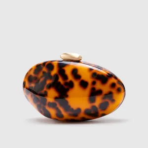 Macro shot of amber tortoiseshell acrylic clutch featuring a matte gold spherical metal clasp