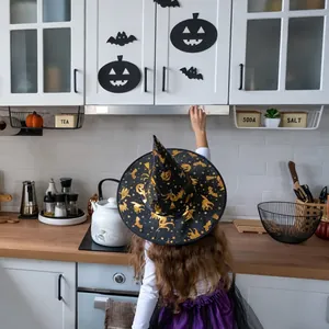 Detail of Halloween witch hat with gold foil pumpkin patterns worn by a child in a kitchen