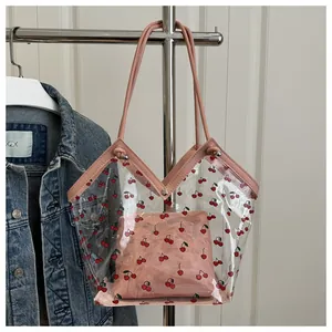Detailed view of clear PVC tote bag with cherry print and pink handle on hanger