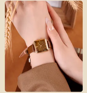Primer plano de un reloj cuadrado dorado con correa de cuero marrón en la muñeca