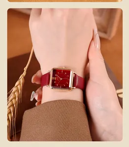 Vista detallada del reloj cuadrado vintage con correa de cuero rojo en la muñeca de la modelo