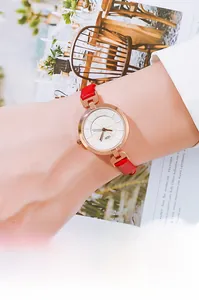 Elegant ladies watch with red leather strap and rose gold case on a wrist with magazine