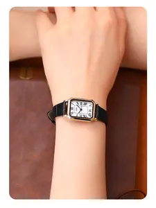 Wrist view of a vintage rectangular gold watch with Roman numerals and black leather strap