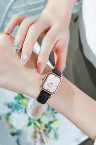Square rose gold watch with black leather strap on a wrist with floral background