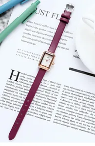 Gros plan d'une montre rectangulaire en or rose avec bracelet en cuir bordeaux sur revue