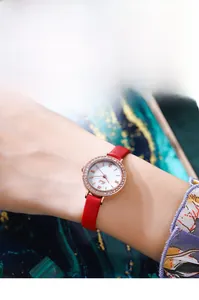 Gros plan d'une montre élégante en or rose avec diamants et bracelet en cuir rouge au poignet