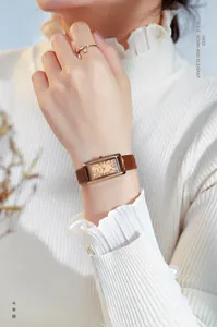 Nahaufnahme einer rechteckigen Quarzuhr mit Roségoldgehäuse und braunem Lederarmband am Handgelenk