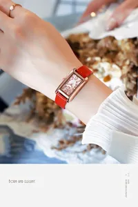Nahaufnahme der eleganten roségoldenen Rechteck-Uhr mit rotem Krokodillederband am Handgelenk