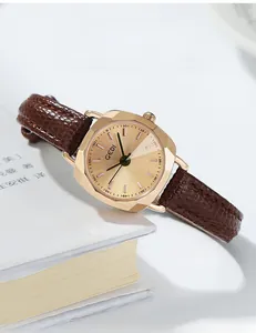 Détail de la montre GEDI dorée rectangulaire avec bracelet en cuir brun sur un livre