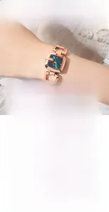 Détail de la montre carrée en or rose avec cadran vert paon et bracelet en métal