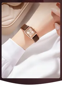 Gros plan d'une montre rectangulaire or rose avec bracelet en cuir marron au poignet