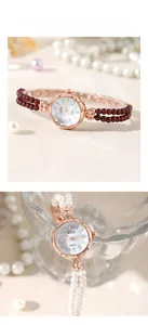 Makroaufnahme einer roségoldenen Quarzuhr mit Perlenarmband und Zifferblatt mit Kristallen