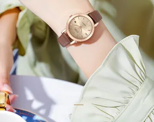 Close-up of a women's quartz watch with a gold dial and brown leather strap on wrist