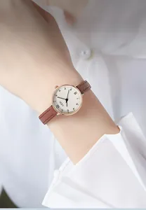 Close-up of minimalist quartz watch with brown leather strap worn on female wrist