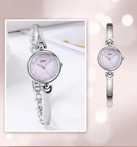Detalle de reloj tipo brazalete plateado con esfera rosa claro e índices de circonita
