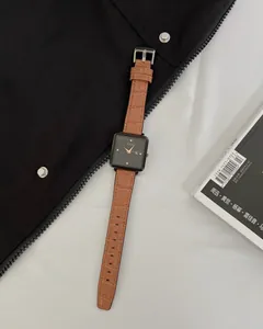 Detail of square black watch dial with rose gold hands and brown crocodile leather strap