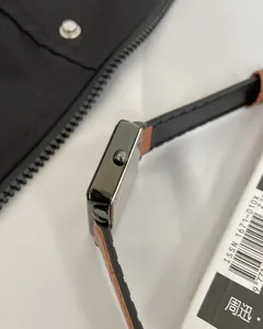 Side view of square metal watch case with crown and two-tone leather strap detail