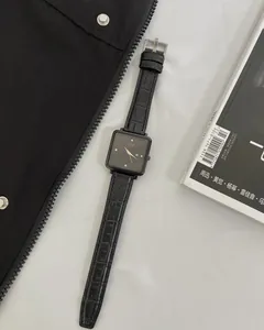 Detail view of square black watch dial with crystal indices and leather strap on magazine