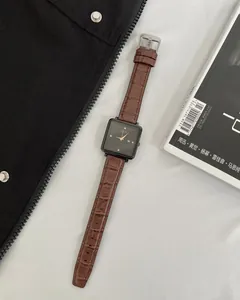Detail of square black dial watch with brown crocodile pattern leather strap on magazines
