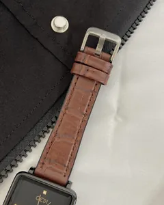 Detail shot of rectangular black watch face and brown crocodile texture strap