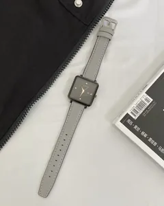 Flat lay of a square GEDI quartz watch with black dial and grey leather strap on a magazine